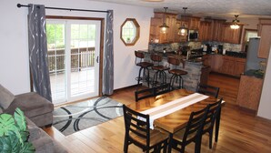 Un comedor con una mesa y sillas de madera, una cocina con armarios de madera y un ventanal corredizo que da a una terraza.
