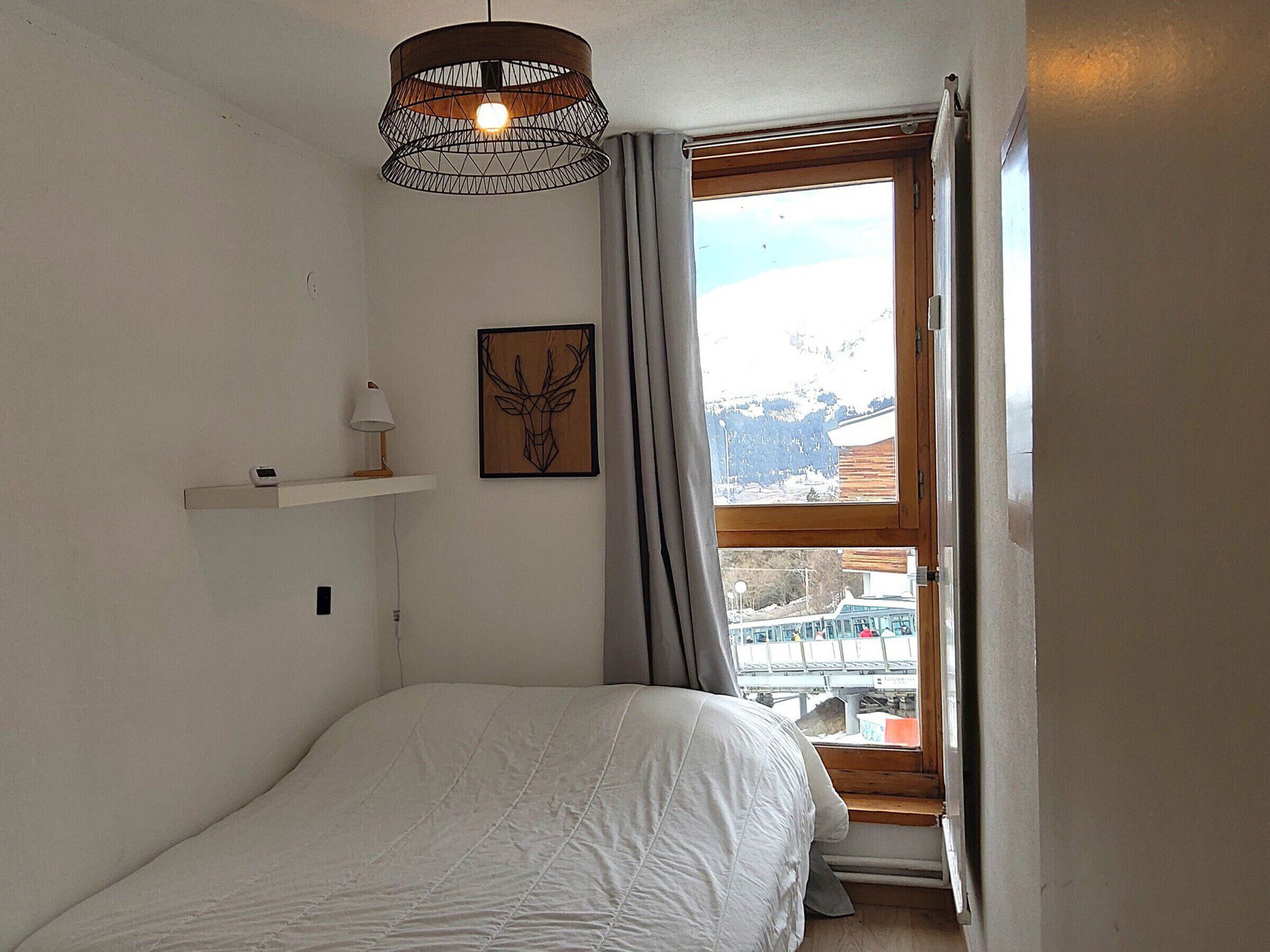Et soveværelse med en seng, en vægmonteret lampe, et indrammet billede og et vindue med gardiner.