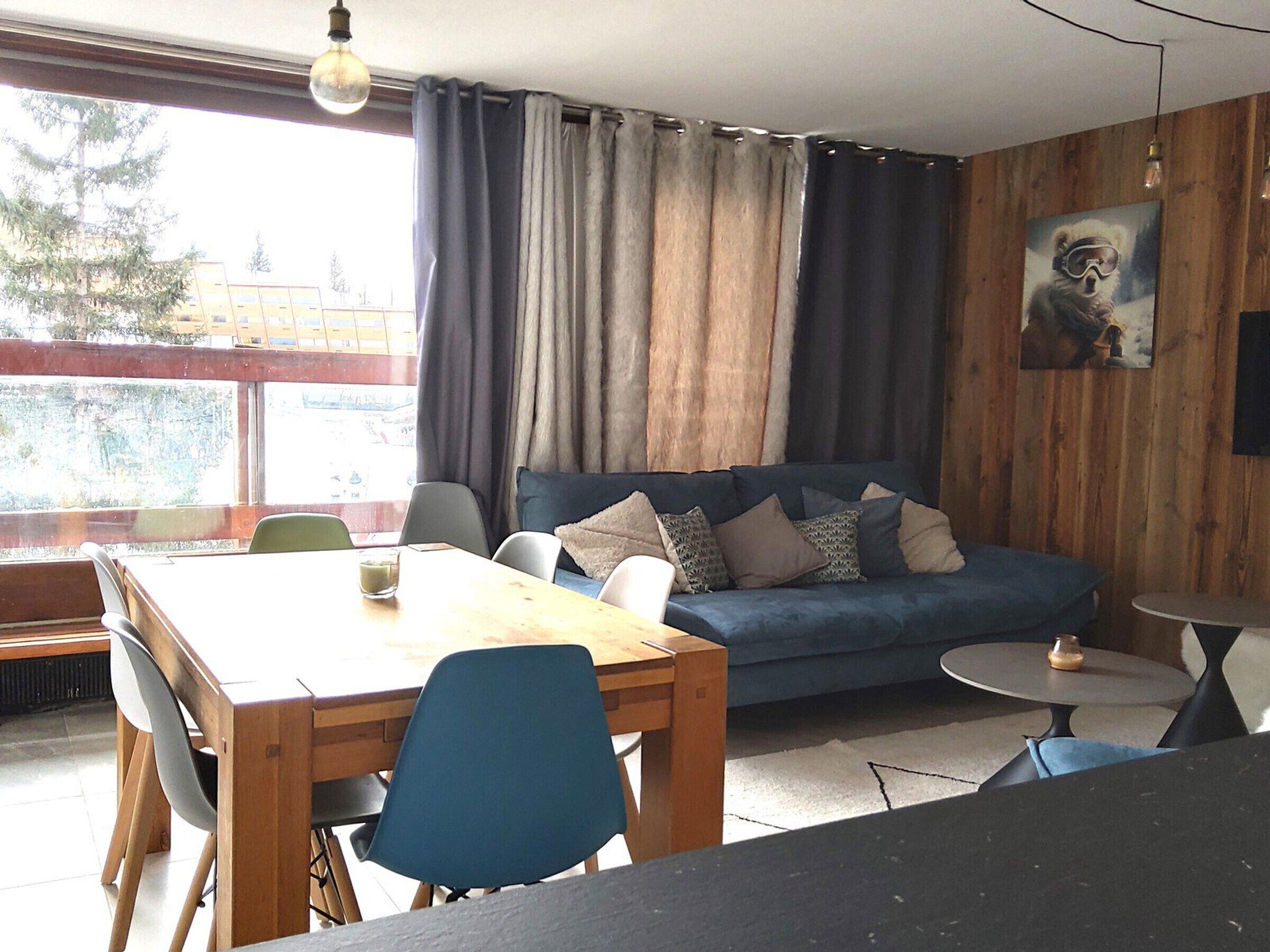 Une pièce avec un mur en bois, un canapé bleu, une table à manger en bois avec des chaises, et une petite table ronde.