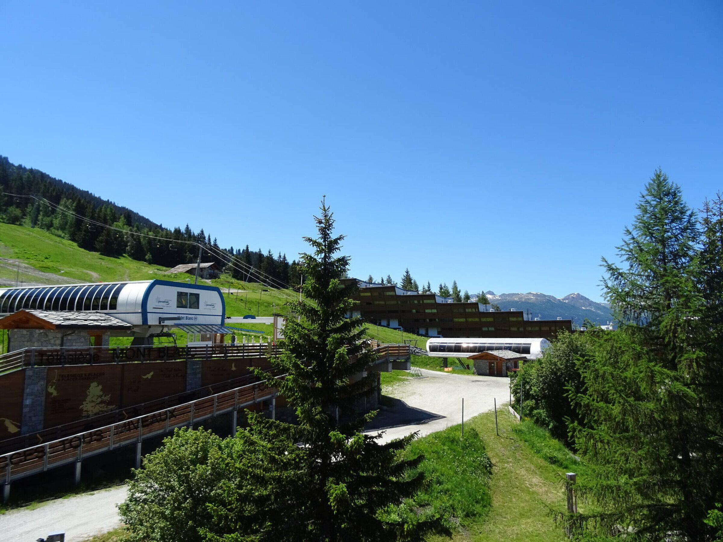 A modern building with a ski lift in the background, surrounded by greenery and mountains.