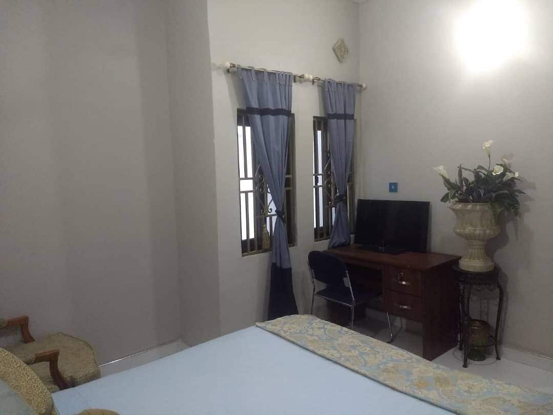 A bedroom with a bed, a desk, a chair, and a potted plant.