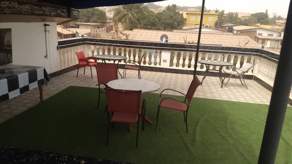 Een balkon met een groen tapijt, rode stoelen en een ronde tafel.