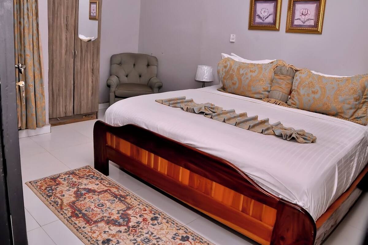 Een slaapkamer met een groot bed, een stoel, een vloerkleed en een kledingkast.