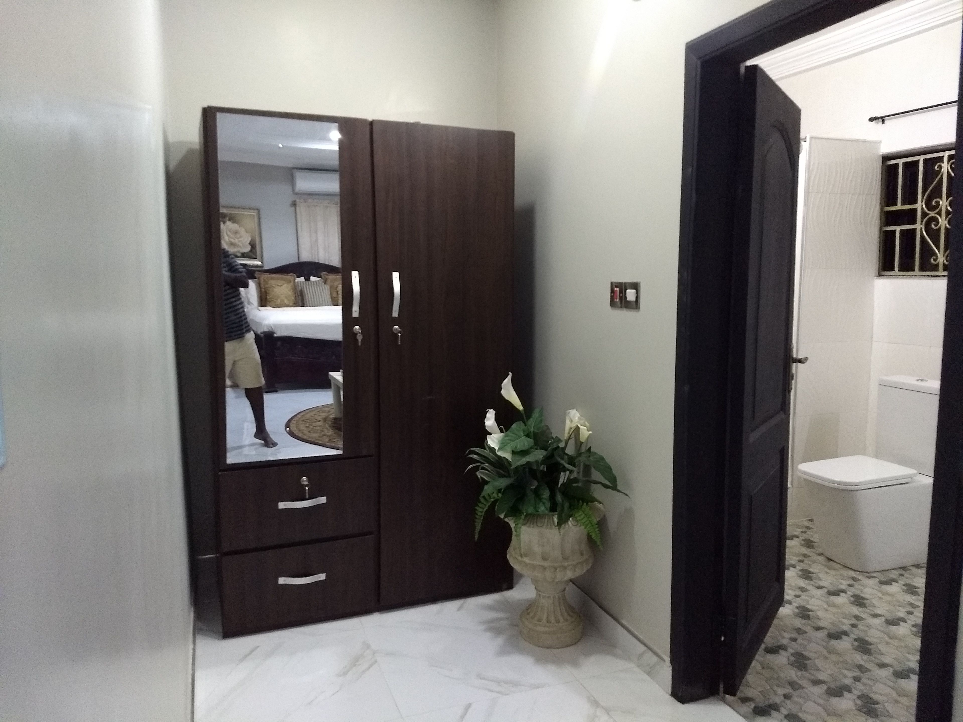 A bedroom with a large wardrobe, a bed, and a potted plant.