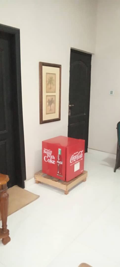 A room with a door, a framed picture on the wall, and a red Coca-Cola cooler on a wooden stand.