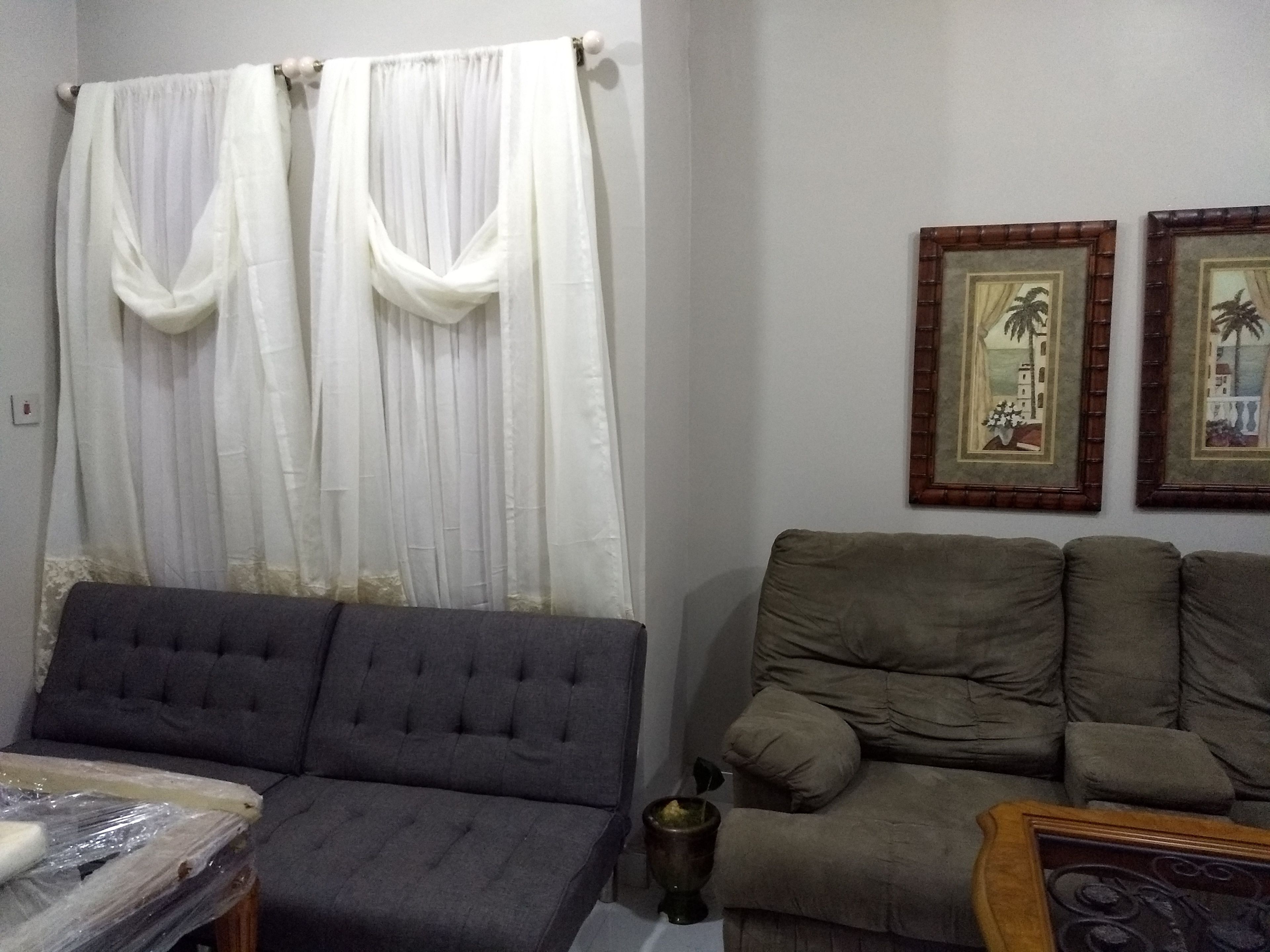 Una sala de estar con un sofá gris, un sillón gris más pequeño y una mesa de centro de madera. Hay dos cuadros enmarcados en la pared.
