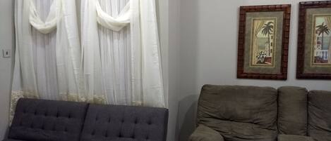 Una sala de estar con un sofá gris, un sillón gris más pequeño y una mesa de centro de madera. Hay dos cuadros enmarcados en la pared.