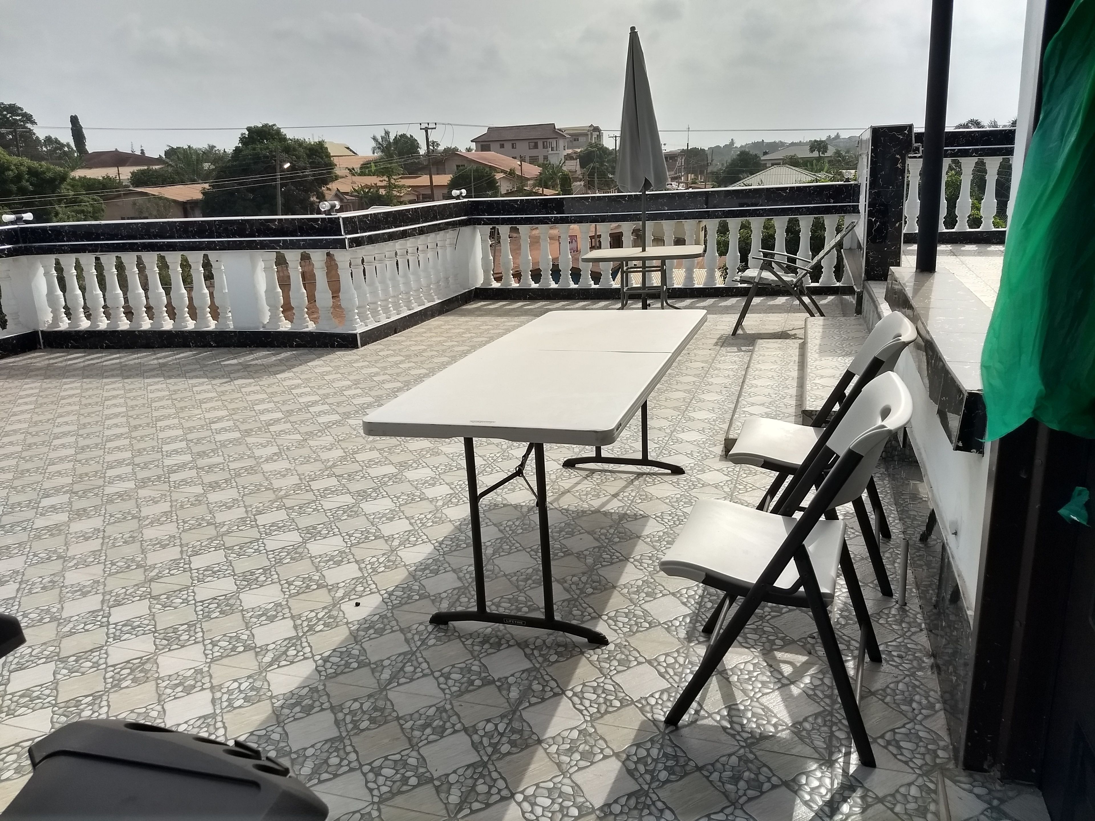 Una terraza en la azotea con suelo de baldosas, barandilla blanca y una mesa con sillas.