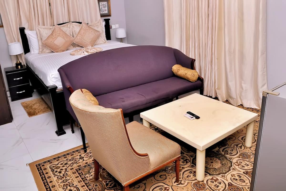 Een hotelkamer met een bed, een paarse bank, een houten fauteuil, een kleine tafel en een nachtkastje.