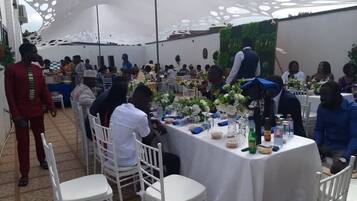Un salón de banquetes con mesas redondas cubiertas con manteles blancos, sillas blancas y centros de mesa florales.