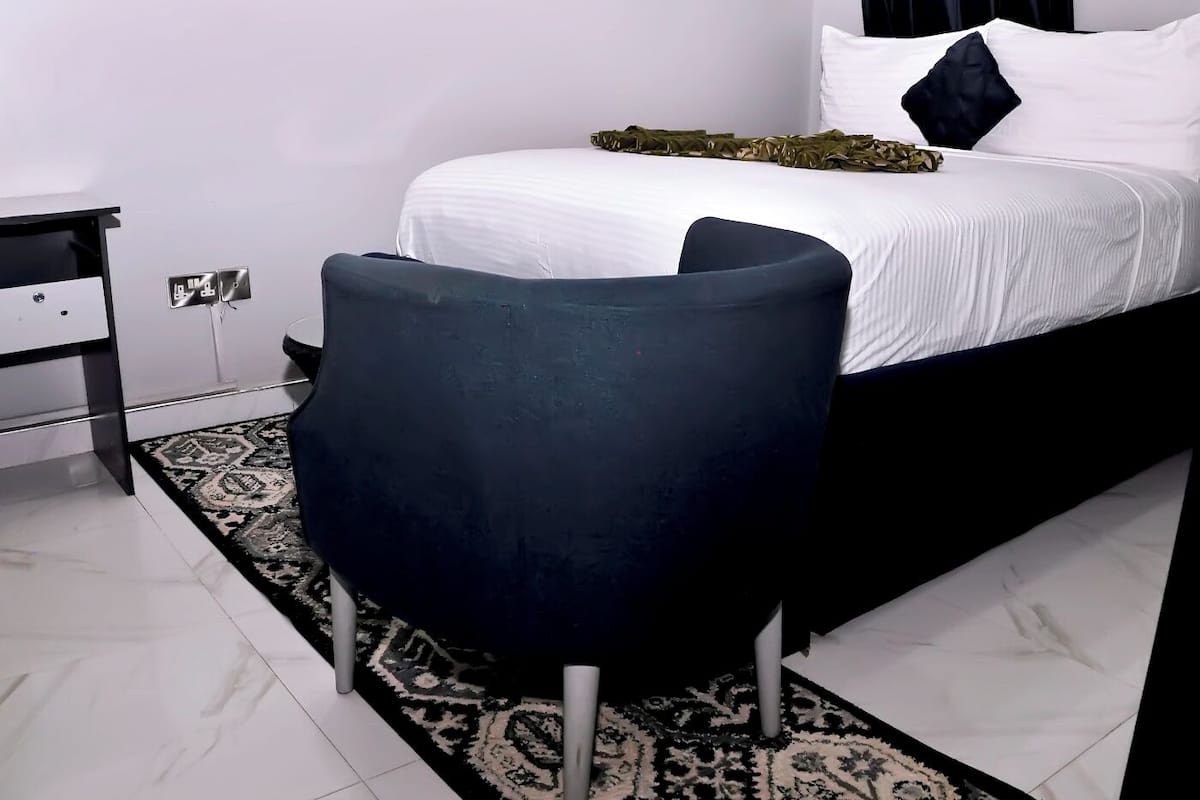 Een moderne hotelkamer met een bed, een klein nachtkastje, een stoel en een kamerkleed met dessin.