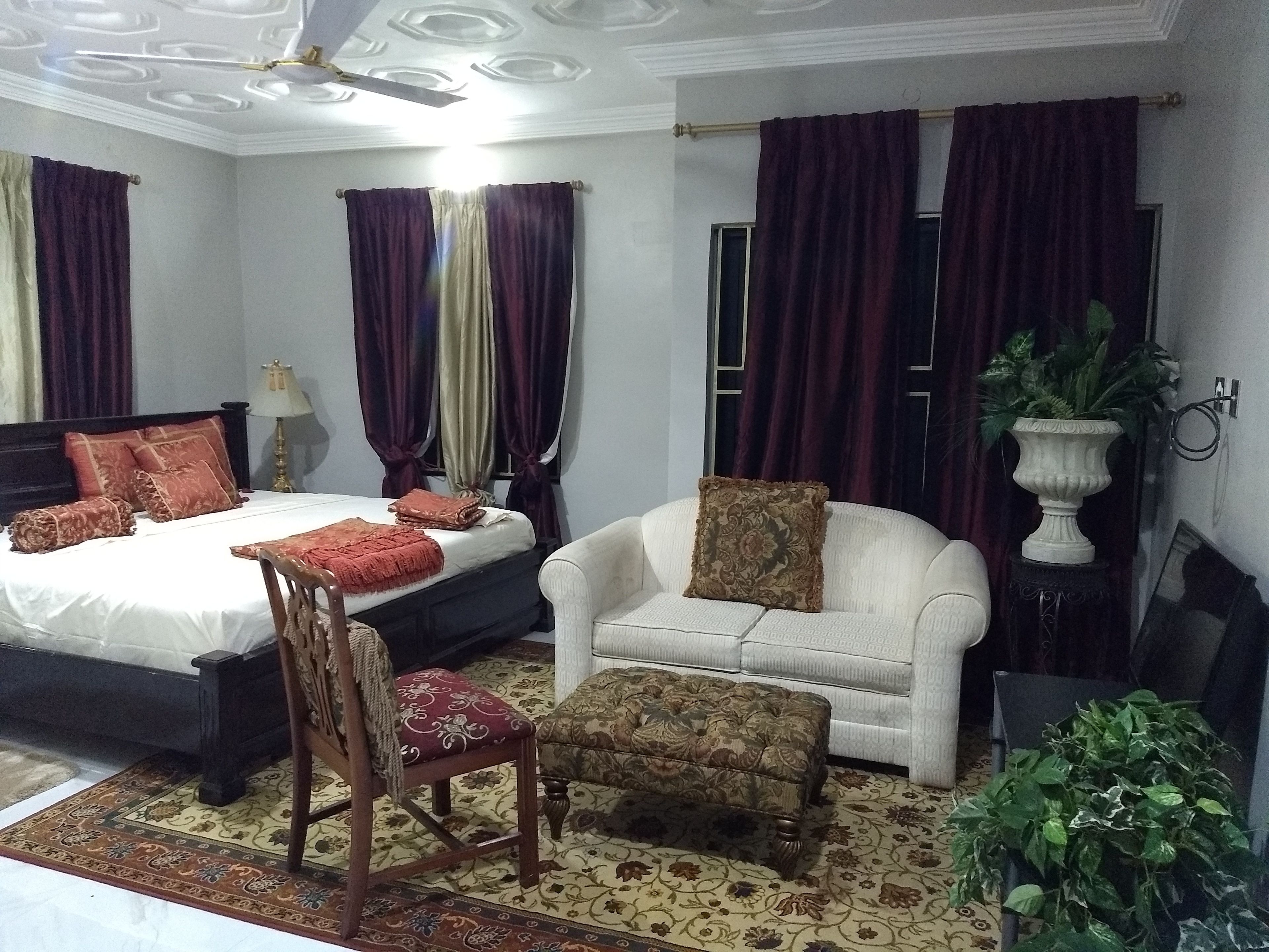 A hotel room with a bed, a sofa, a chair, a small table, and a potted plant.