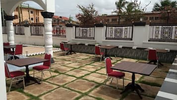 Un área de estar al aire libre con mesas y sillas, suelo de baldosas y una pared blanca con detalles decorativos.