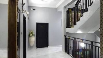 Un pasillo con una puerta negra, una planta en maceta y una escalera con barandillas ornamentales.