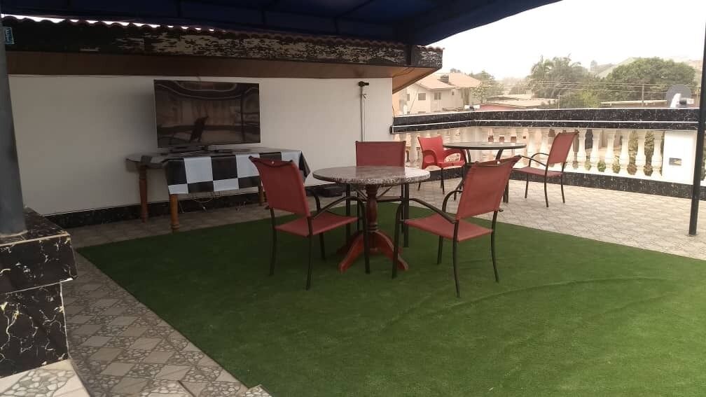 Une terrasse extérieure avec une table ronde et des chaises rouges, une nappe à carreaux et un barbecue.