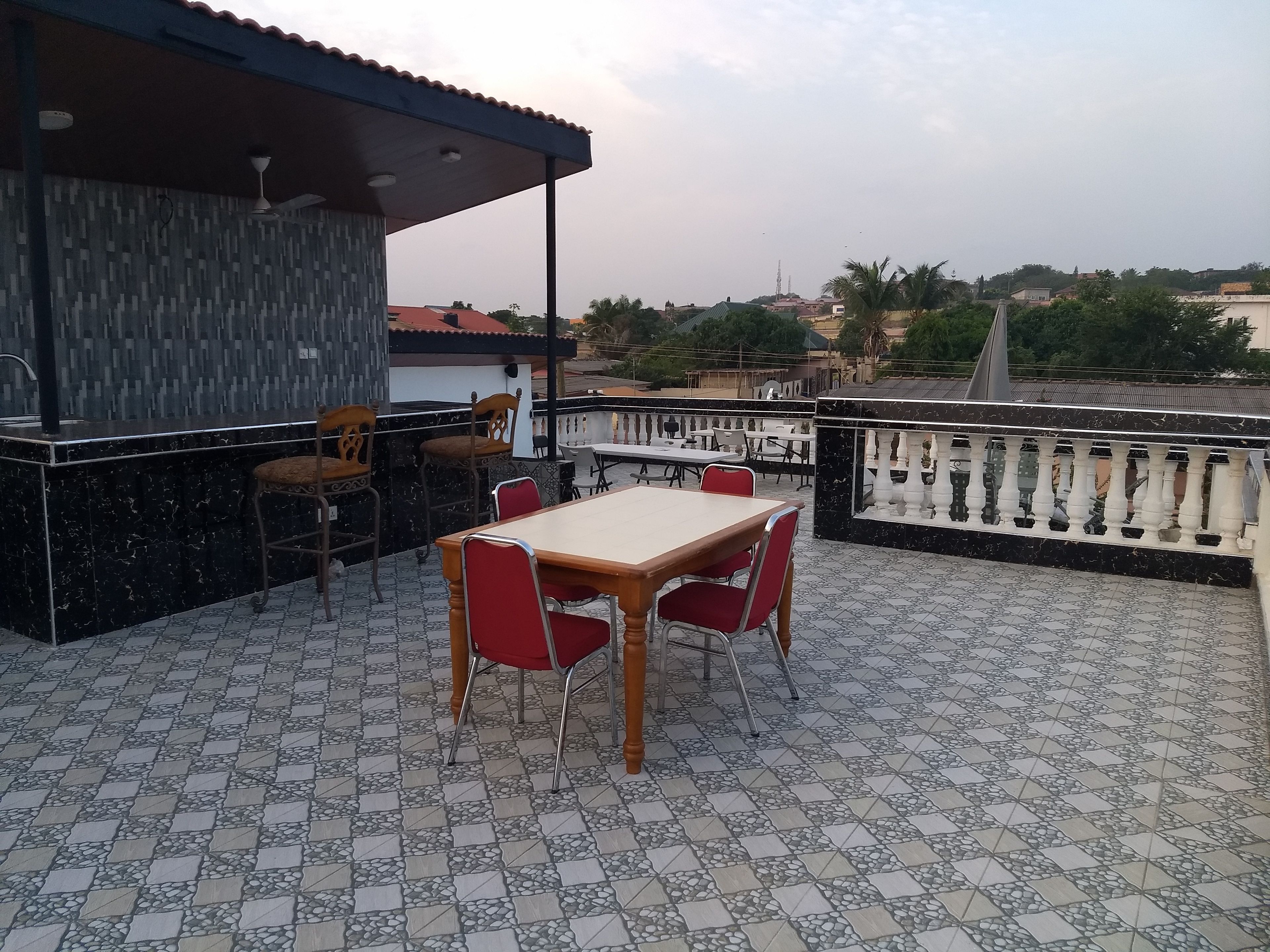 Eine Terrasse mit Tisch und Stühlen, ein Barbereich und Blick auf die umliegenden Gebäude und die Landschaft.
