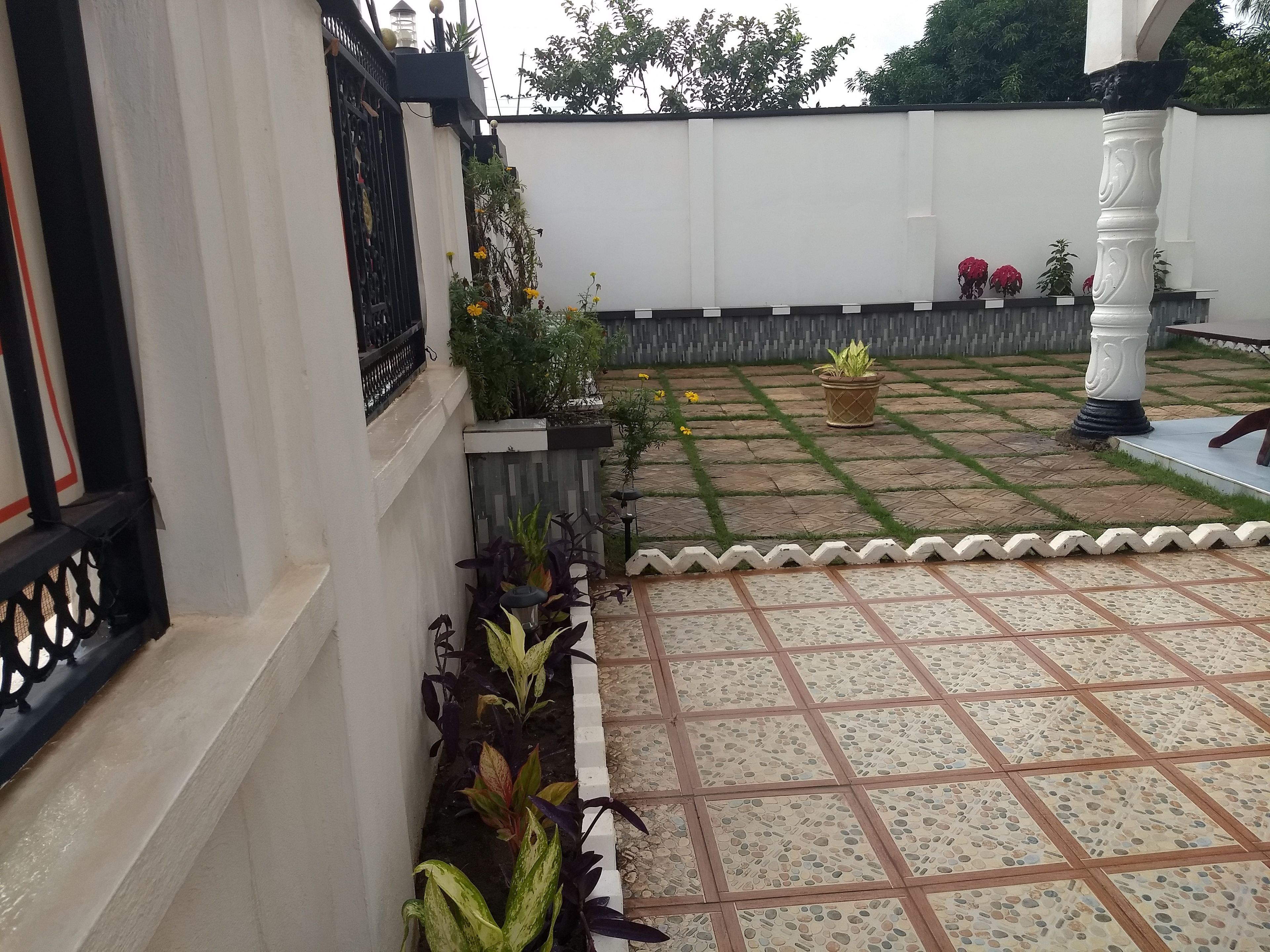 Un patio con suelo de baldosas, pared blanca y portón de metal negro.