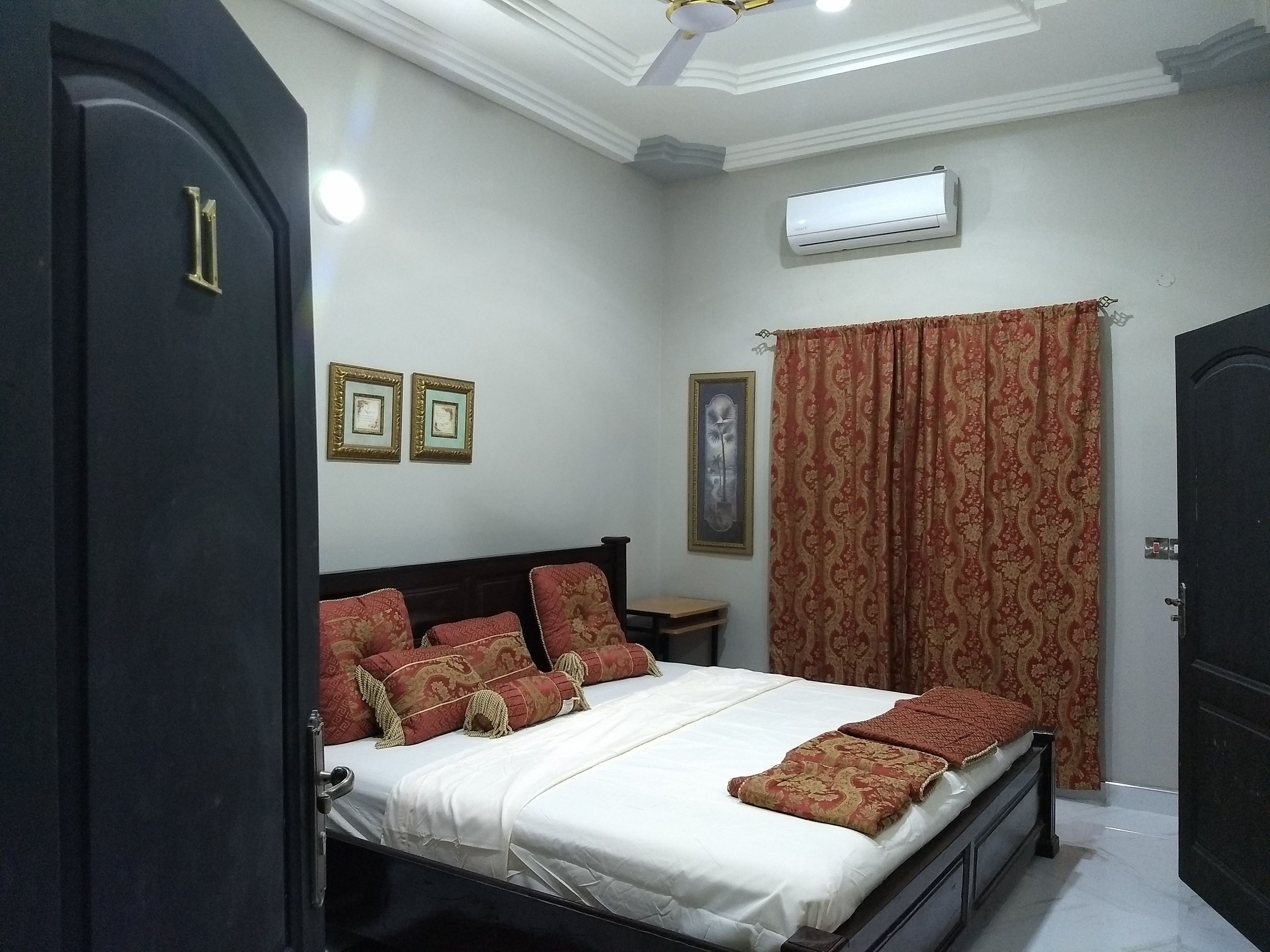 A bedroom with a bed, a nightstand, an air conditioning unit, and a door.
