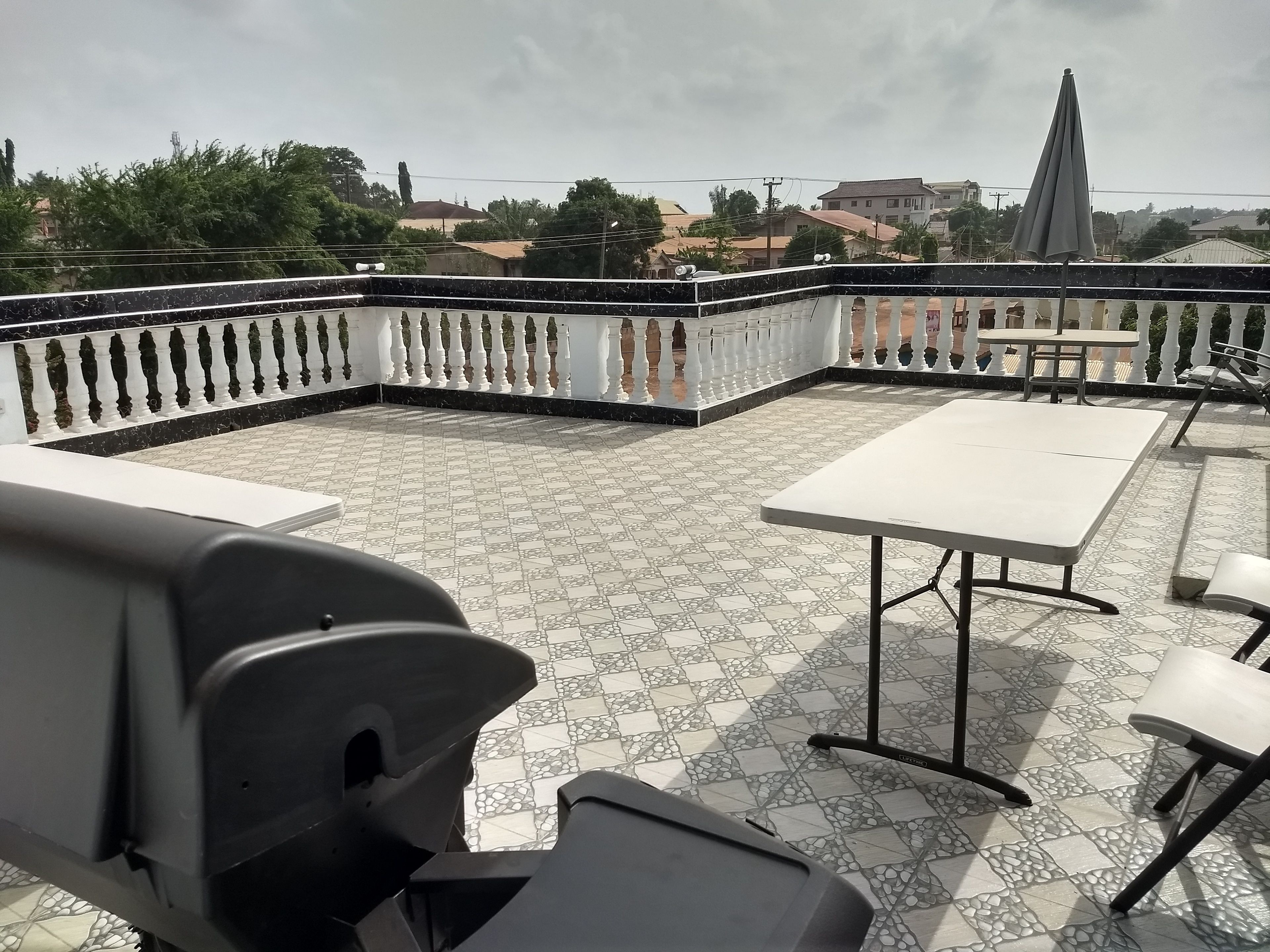 An outdoor patio with a tiled floor, white and black chairs, and a table.