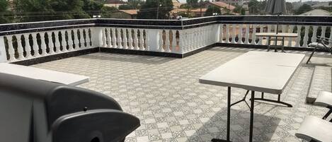 An outdoor patio with a tiled floor, white and black chairs, and a table.