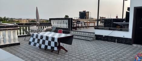 A rooftop terrace with a checkered table, chairs, and a water tank in the background.