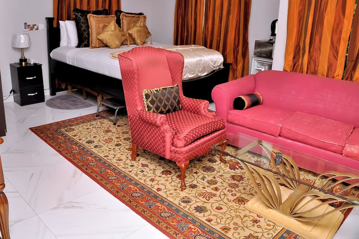 Een slaapkamer met een bed, een rode fauteuil, een roze bank, een glazen salontafel en een kamerbreed tapijt met een patroon.