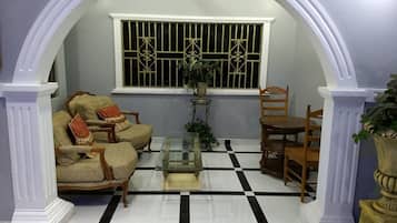 A room with a checkered floor, a sofa set, a dining table, and a window with barred glass.