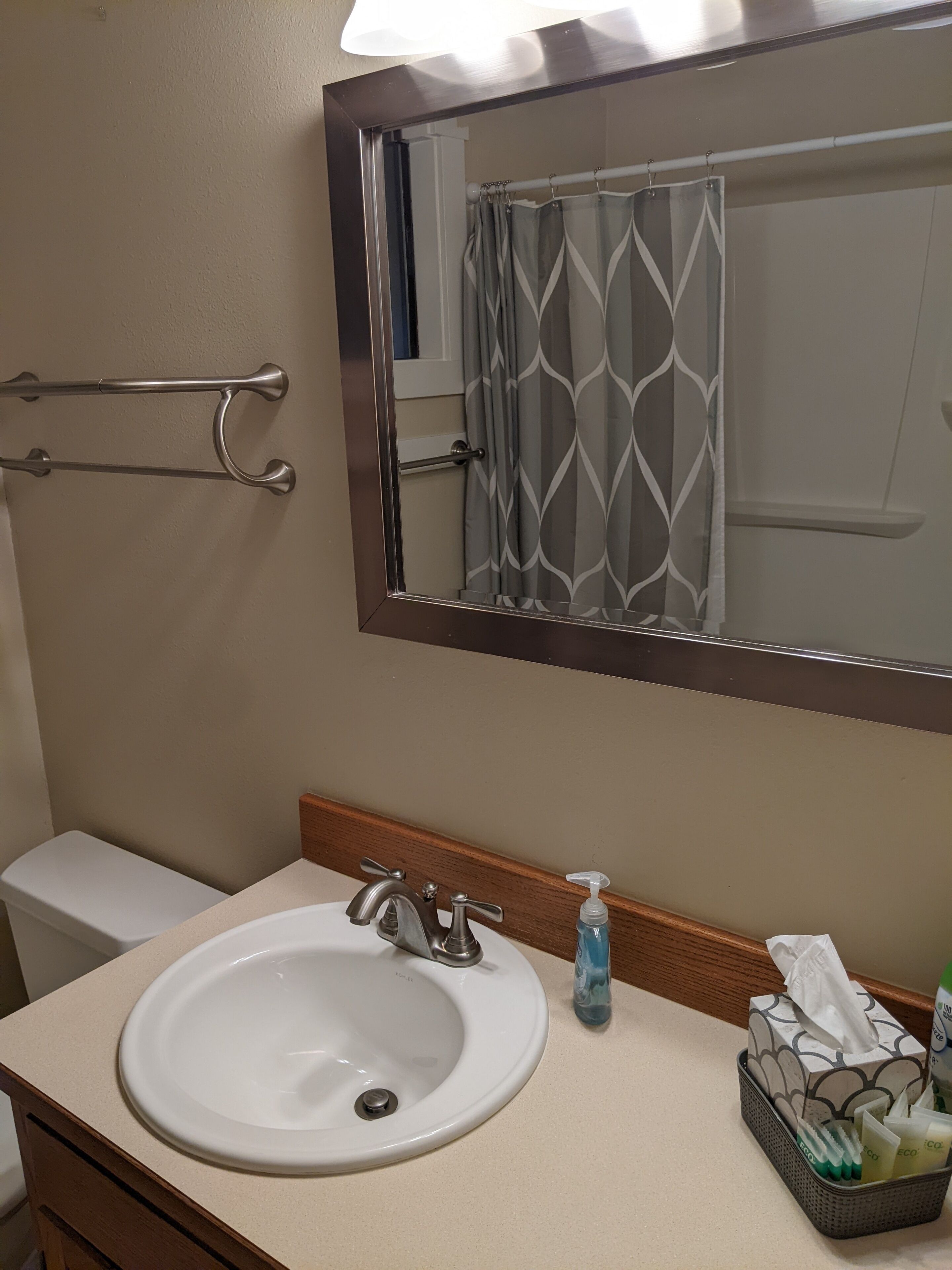 Une salle de bain avec un lavabo blanc, un miroir, un porte-serviettes et un panier contenant des articles de toilette.