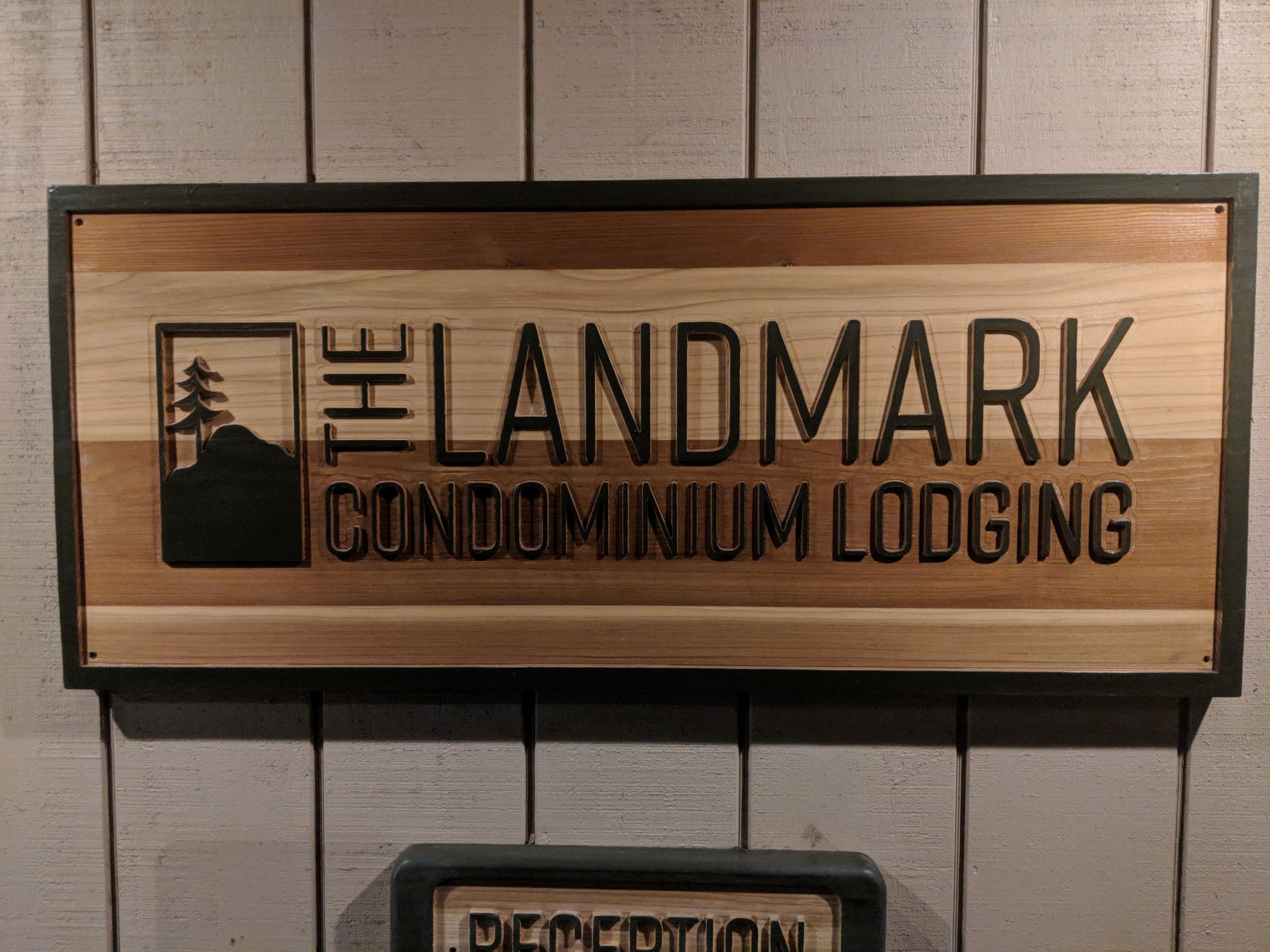 Et træskilt for Landmark Condominium Lodging med et bjerg og et træ som ikon.