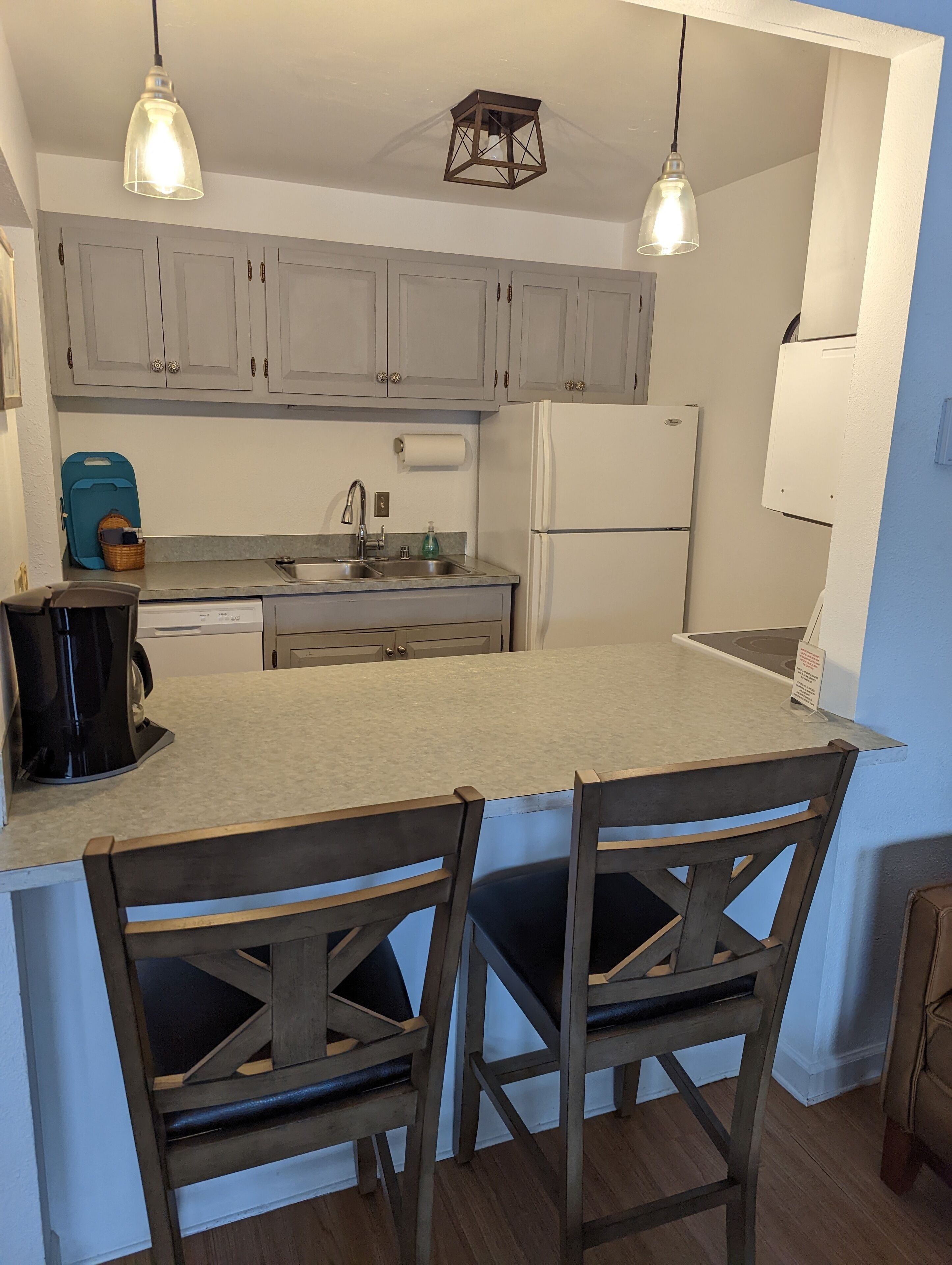 A kitchen with a central island, two wooden chairs, a coffee maker, and a refrigerator.