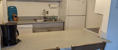 A kitchen with a central island, two wooden chairs, a coffee maker, and a refrigerator.