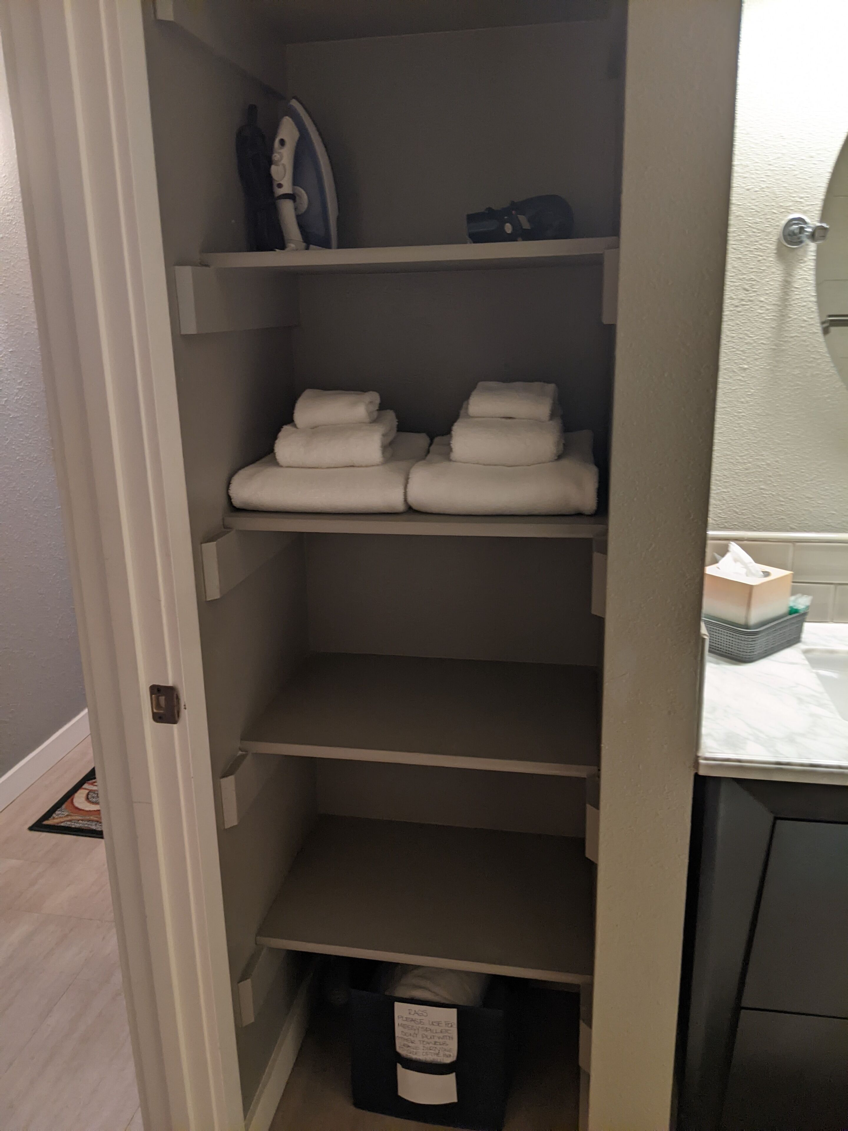 A closet with shelves holding folded towels and a basket with a tag.