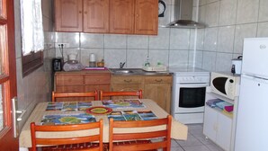 A kitchen with wooden cabinets, a dining table with chairs, a stove, a microwave, and a refrigerator. - La Rivière St Louis, 2-room apartment "Furnished tourist accommodation 3 *** (Le Ouaki)