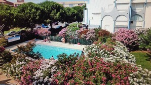 A swimming pool surrounded by lush gardens with various flowering plants. - Studio Pool Parking (Le Grau-du-Roi)