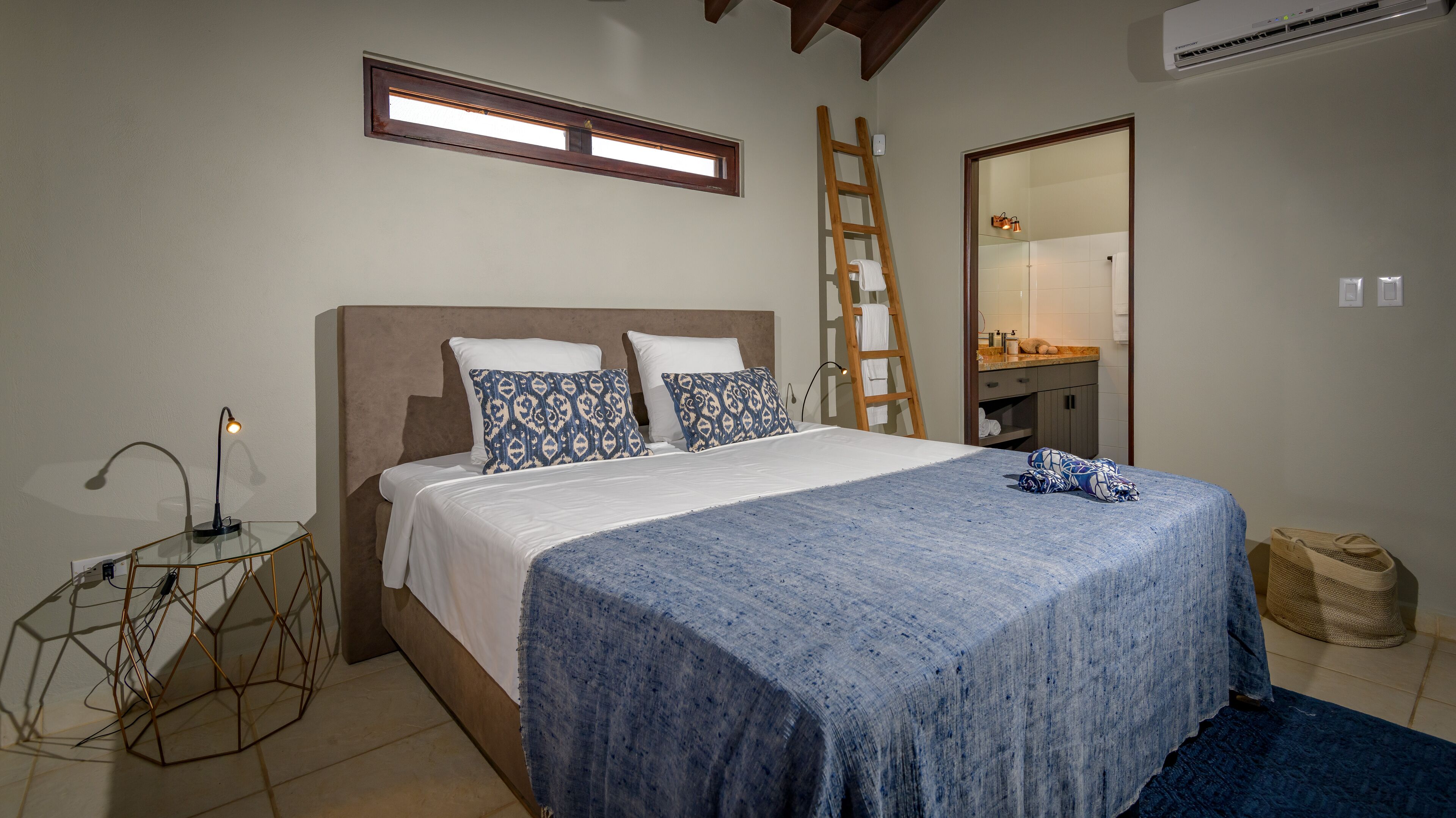 Un dormitorio con cama, mesita de noche, escalera, espejo y baño pequeño.