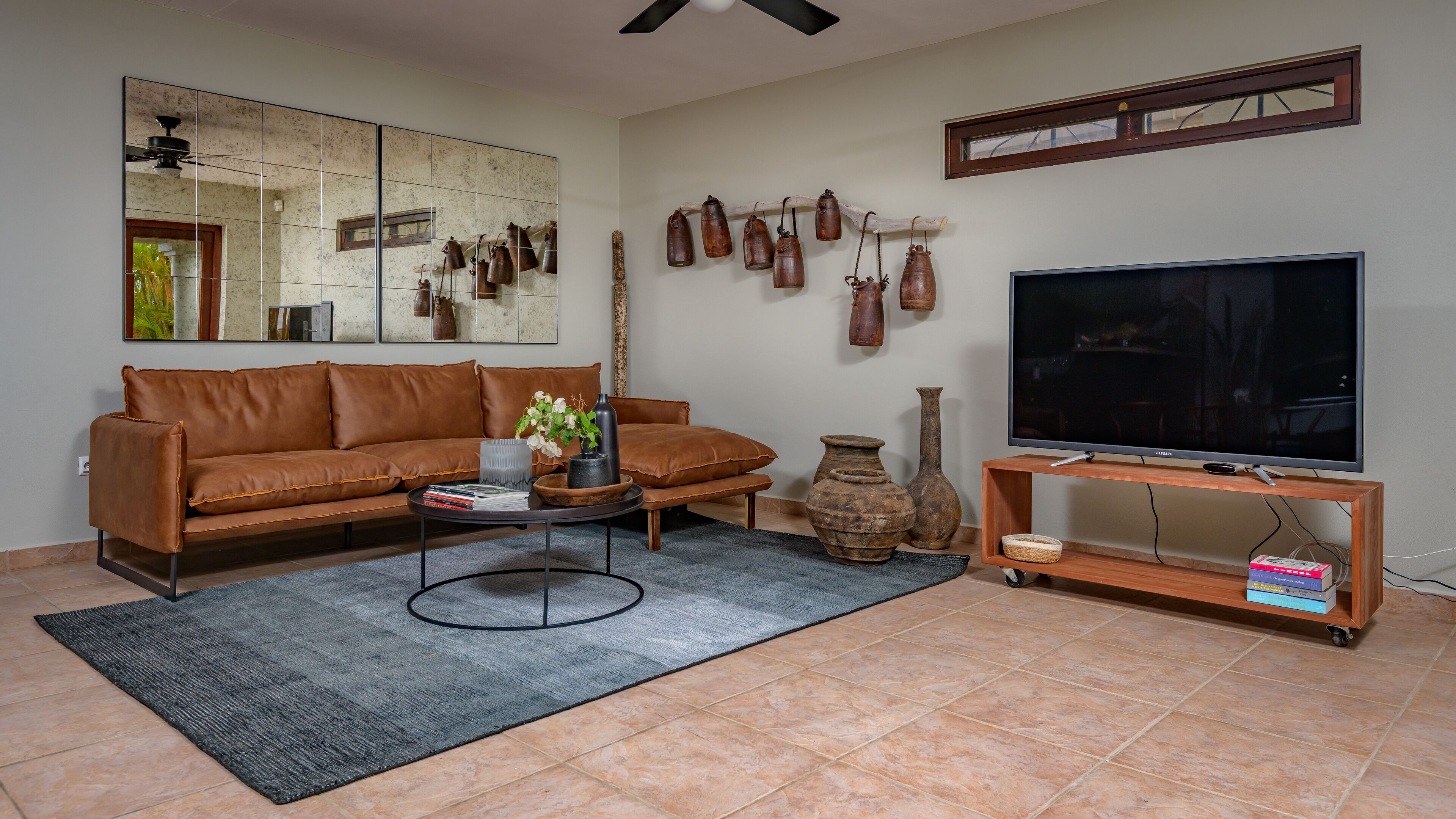 A living room with a brown leather sofa, a coffee table, a TV on a wooden stand, and a large mirror on the wall.