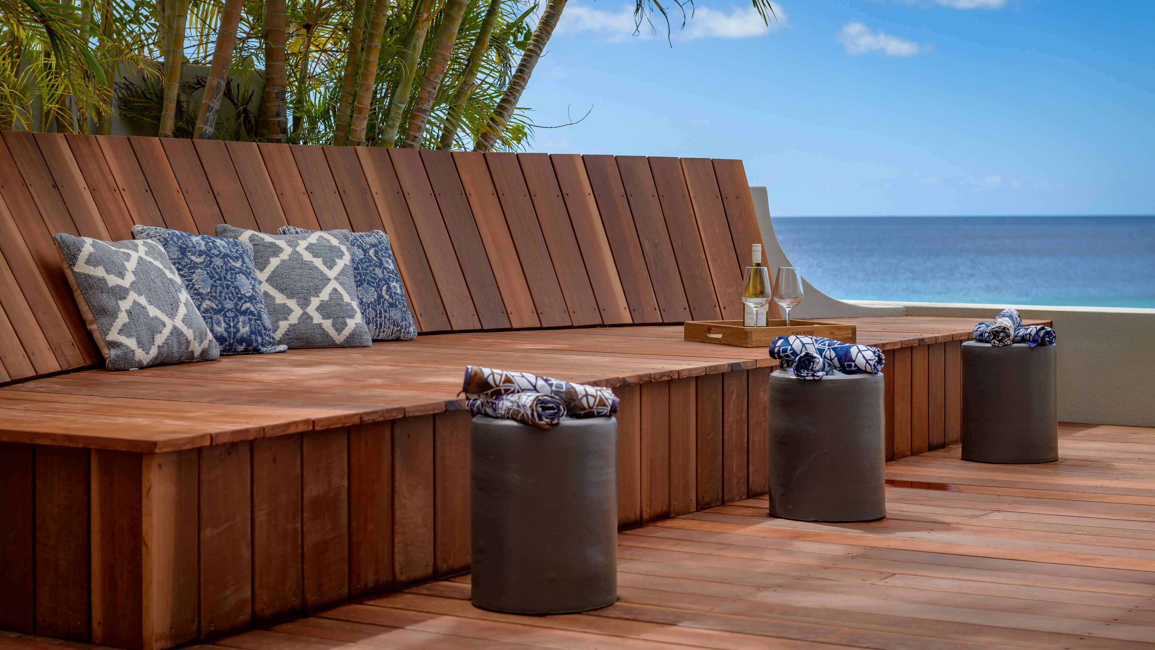 A wooden deck with a curved seating area, a small table with a tray, and a view of the ocean.