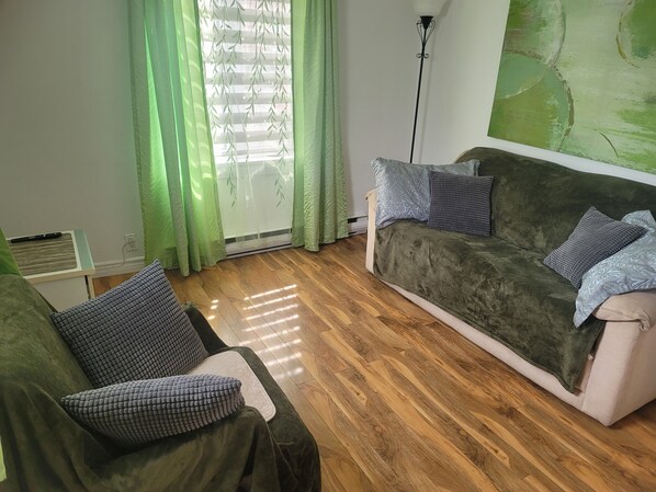 Un salon avec un canapé vert, des coussins à motifs, un plancher en bois et un rideau vert.