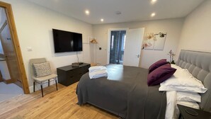 Une chambre moderne avec un grand lit, un téléviseur fixé au mur, une table de chevet et une chaise.