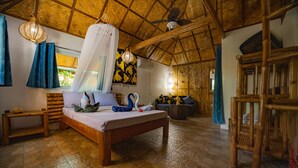 Una habitación con una cama, un banco de madera, una lámpara colgante y un techo tejido.