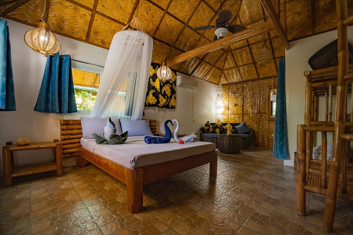 A room with a bed, a wooden bench, a hanging light fixture, and a woven ceiling.