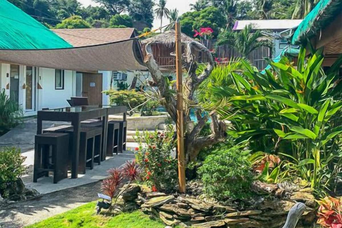 A tropical garden with a dining area, a large tree sculpture, and a house with a green roof.