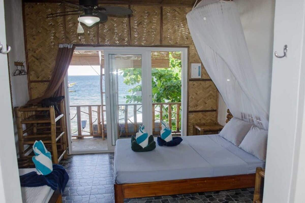 A room with a bed, a chair, a table, and a view of the sea through a glass door.