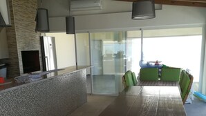 A modern kitchen with a large wooden dining table, a built-in island, and a seating area with green chairs. - HOUSE WITH SWIMMING POOL AND BARBECUE (Vila Boim)