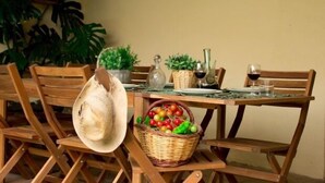 A dining table with chairs, a basket of fruit, a hat, and a wine bottle. - Self catering Cal Cabrer for 12 people (Sant Jaume dels Domenys)