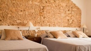 A bedroom with two beds, a stone wall, and a nightstand with a lamp. - Self catering Cal Cabrer for 12 people (Sant Jaume dels Domenys)
