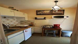 Uma cozinha compacta com pia, torradeira, cafeteira e um pequeno banquinho.
