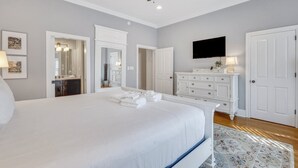 Een slaapkamer met een groot bed, een plafondventilator, een aan de muur bevestigde televisie en een dressoir.