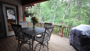 Une terrasse en bois avec une table et des chaises, un barbecue et une vue sur les arbres.