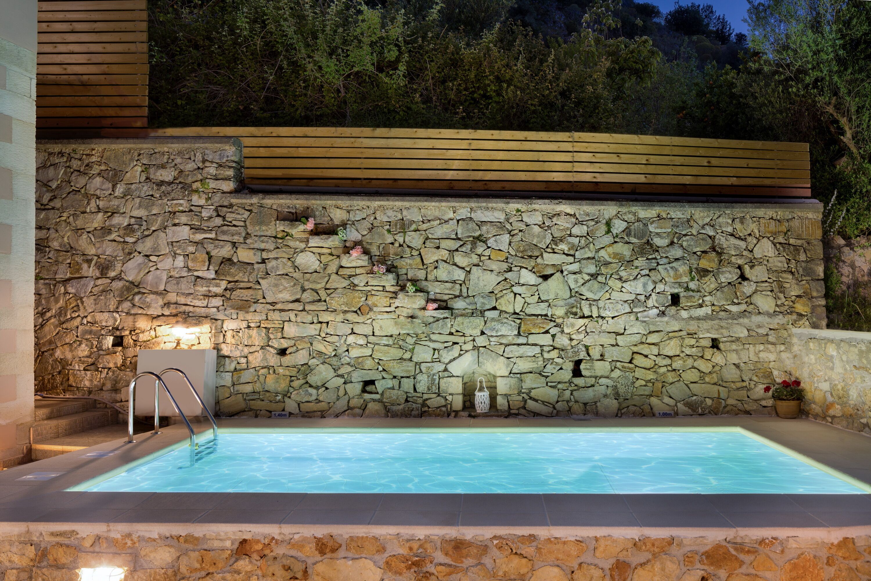 A swimming pool with stone walls and wooden deck, surrounded by greenery.
